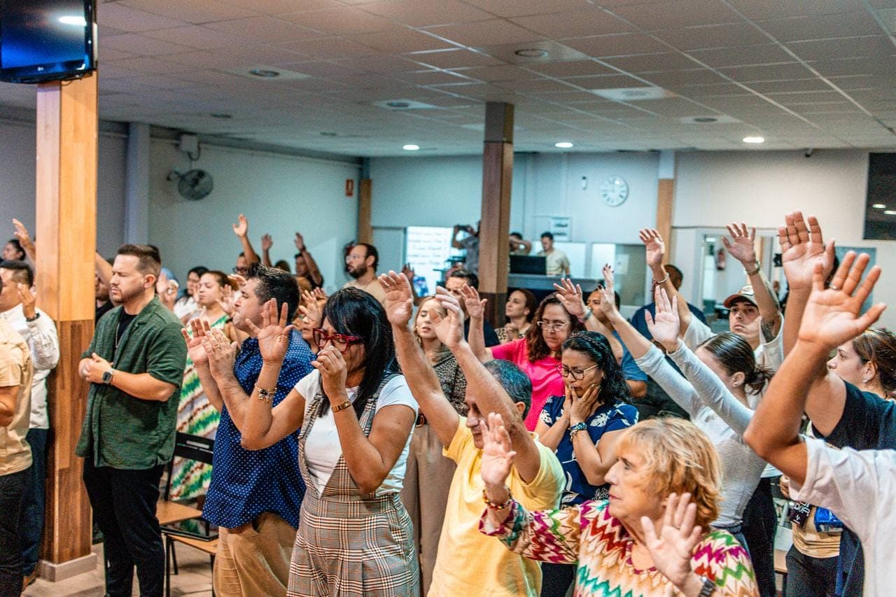 Asistentes de pie en adoración, con las manos levantadas y los ojos cerrados
